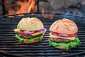 Two homemade hamburgers on a barbecue with fire