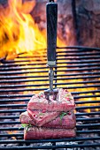 Steaks auf Fleischgabel auf dem Grill mit Rosmarin und Pfeffer