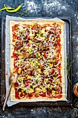 An unbaked pizza with pulled pork, sweetcorn, pineapple and onion on a baking sheet