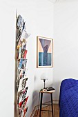 Bar stool used as bedside table between postcard rack and framed picture on wall