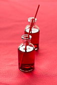 Cranberry juice with straws in small glass bottles on a red surface
