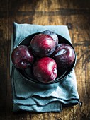 Plums in a bowl on a wooden surface