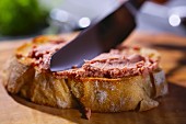 Liver pâté being spread on a slice of baguette