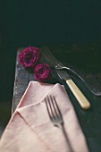 Still-life arrangement of cutlery, pink napkin and roses