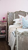 Antique grey bed with cane headboard and foot against pink wallpaper