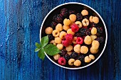 Bowl of colorful yellow and red raspberries and black dewberry with leaf