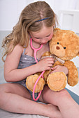 Girl using stethoscope with teddy bear