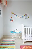 Kinderzimmer mit weißem Gitterbett, hellblauem Beistelltisch und pastellfarbener Girlande mit Elefanten-Motiven