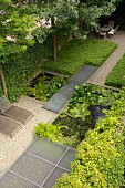 Geometrisch angelegter Garten mit Teich, Gittersteg, Bodendeckern und Outdoormöbeln
