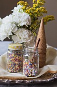 Colourful sprinkles in preserving jars, ice cream cones and flowers