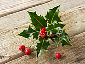 Fresh holly leaves with red berries on a wooden surface