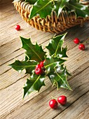 Holly leaves with red berries in a basket on a wooden surface
