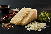 Ein Stück Asiago-Käse, Basilikum und Gewürze auf Schiefertafel