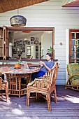 Young woman sitting on the porch with rattan furniture in front of the window