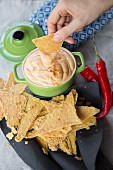 A hand dipping a nacho into cheddar and chilli dip (vegan)