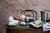 Rustikal gedeckter Tisch mit Zinngeschirr, Käse und Brot vor Backsteinwand