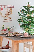 Weihnachtstisch mit Hyazinthen in nostalgischen Tassen, Stollen und Espressokanne, im Hintergrund Tannenbäumchen mit Strohdeko und Girlande aus getrockneten Apfelscheiben an der Wand