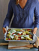 Frau hält Ofenblech mit gebackenem Feta auf Gemüse