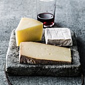 Variety of wedges of cheese on cutting board with red wine