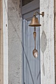 Bell with vintage spoon attached to clapper next to dove-grey front door