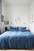 Schmales Schlafzimmer mit blauer Bettwäsche auf Doppelbett und verschiedenen Fotos als Wanddekoration