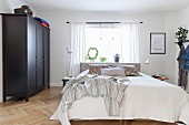 Black wardrobe, herringbone parquet floor and bed below window in bedroom