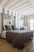 Double bed with headboard made from old fire surround and integrated mirror against striped wall with sink in background