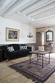 Scatter cushions on black velvet sofa, vintage coffee table and white wood-beamed ceiling in living room