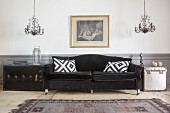 Schwarzes Sofa mit Samtbezug und Kissen, daneben Koffer als Beistelltisch und Kronleuchter