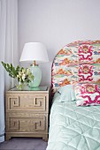 Bedside table with table lamp next to bed with patterned headboard