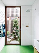 Walk-in shower with glass wall, green floor and door to the courtyard