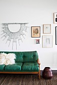 Green retro sofa with fur cushions in front of the picture wall
