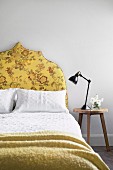 Stool next to the bed with a yellow upholstered headboard