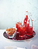 Glasses and bottles of red juice and a bowl of pretzels