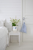 Flowers in old jug on chair used as bedside table