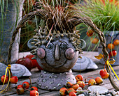 Keramikkopf mit Carex 'Bronce Perfection' (Herbstsegge), als Haare, Malus (Zieräpfel)