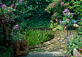 Small pond bordered with clinker, Rosa (rose), Alchemilla (lady's mantle), Petunia (petunia) on blue table, terracotta figure