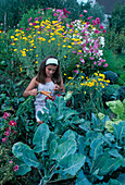 Mädchen mit frisch geerntetem Gemüse im Korb, dahinter hohe Blühpflanzen