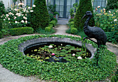 Round water basin with water lilies, metal bird as decoration and ivy as edging
