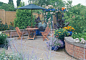 Schön gepflasterte Senk-Terrasse mit gemauerten Terrassenbeeten und Sitzgruppe mit Sonnenschirm