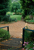 Wooden stairs leading over gravel path into the garden, flower beds bordered with small walls