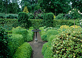 Formaler Garten eingefaßt mit Buxus sempervirens (Buchs), re. u. li. Ilex und im Hintergrund Säulen aus Taxus baccata (Eibe) und Vogeltränke