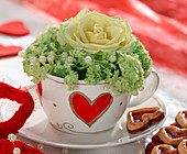 Heart-shaped cup filled with light yellow rose and snowball