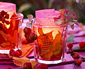Glass windlights filled with autumn leaves, transparent paper