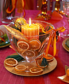 Honey-colored candle in glass cup filled with orange slices