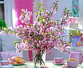 Prunus (ornamental cherry) bouquet in glass vase, pink teacups
