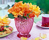 Blossoms of pink (roses, yellow) in pink relief glass on the table, petals