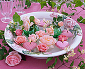 Blüten von rosa Rosa (Rosen), Clematis (Waldrebe), herzförmige Schwimmkerzen