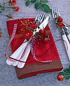 Kleiner Strauß aus Rosa (roten Rosen und Hagebutten) an Besteck auf Serviette
