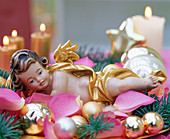 Engel in Bett aus Rosa (Rosenblütenblättern), goldenen Weihnachtsbaumkugeln